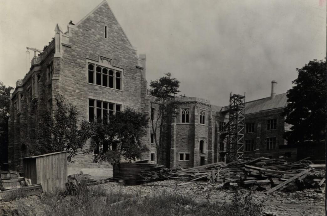 Old photo of the construction of a stone building with scaffolding and building materials in the early stages of development.