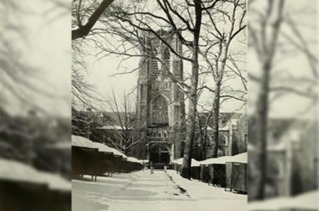 A vintage photo of a stone building with snow draping the front walkway and the roof.