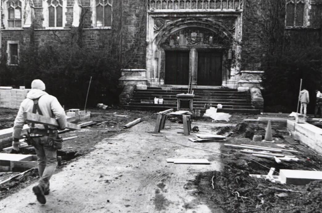 A construction worker walks through the building site of a stone building, surrounded by scaffolding and building materials.