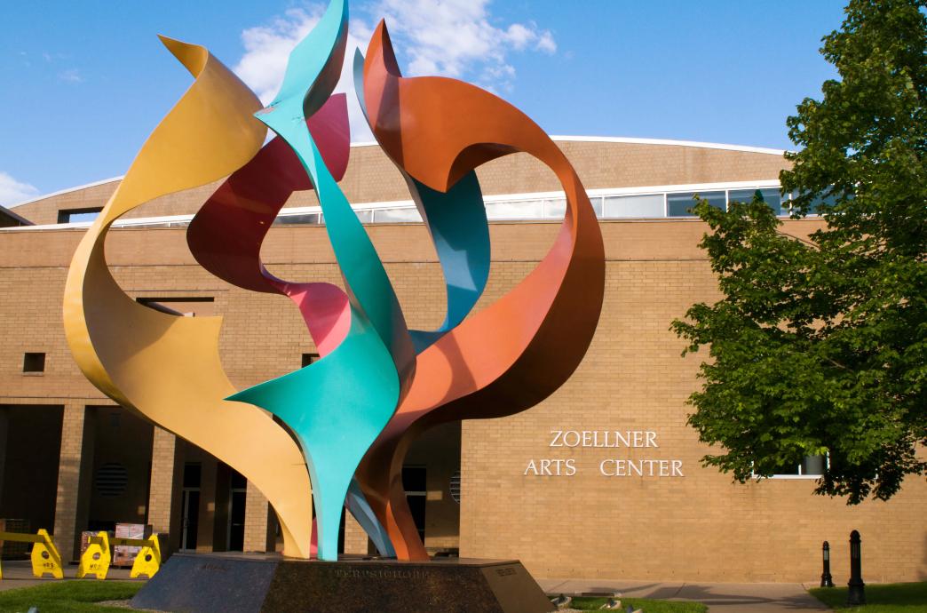 In front of Zoellner Arts Center, a large metal sculpture winding metal in different colors together towards the sky