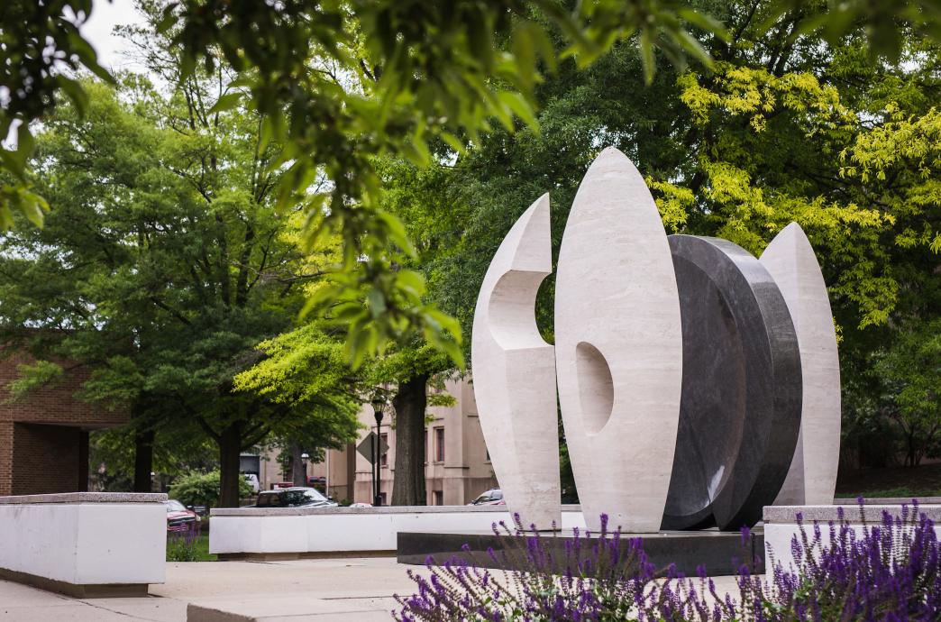 An outdoor stone sculpture in two tones of dark and light gray, stands on campus.