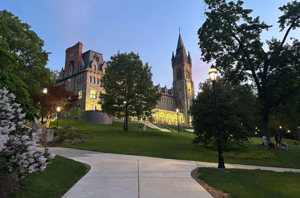 At twilight, the renovated Clayton UC is illuminated and seen from a concrete walkway on the lower part of campus.