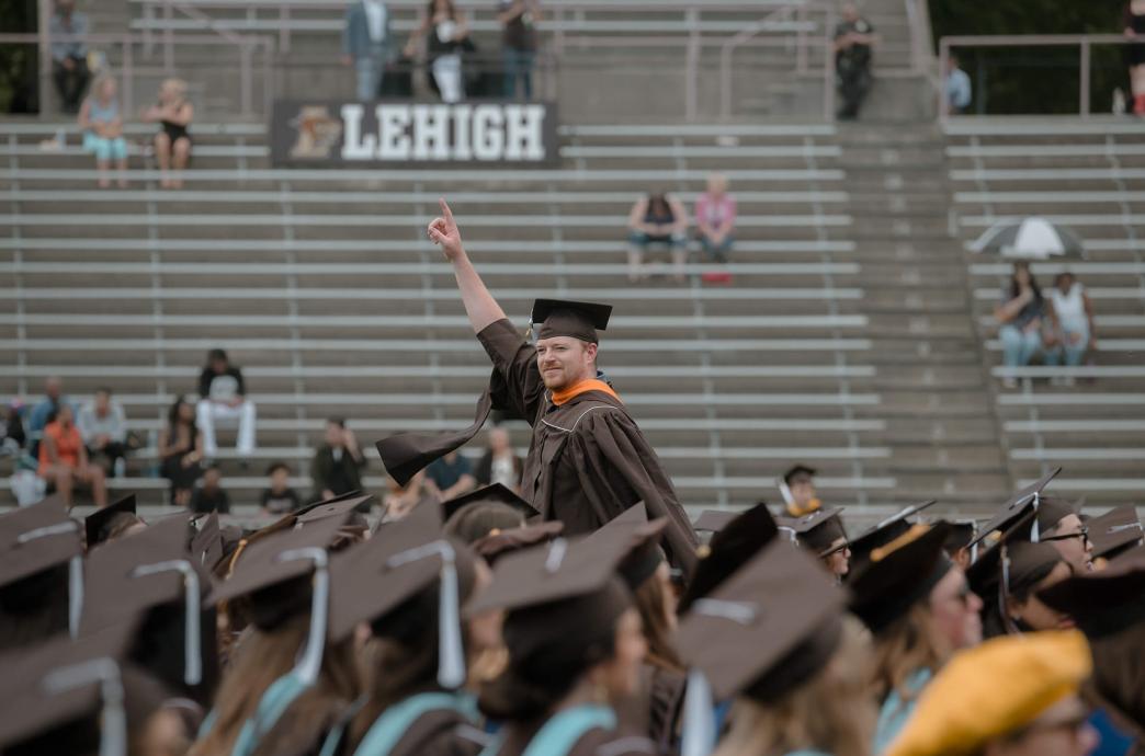 Amid a sea of brown caps, one student stands with one finger raised in the air as a Lehigh sign hangs in the bleachers behind him.