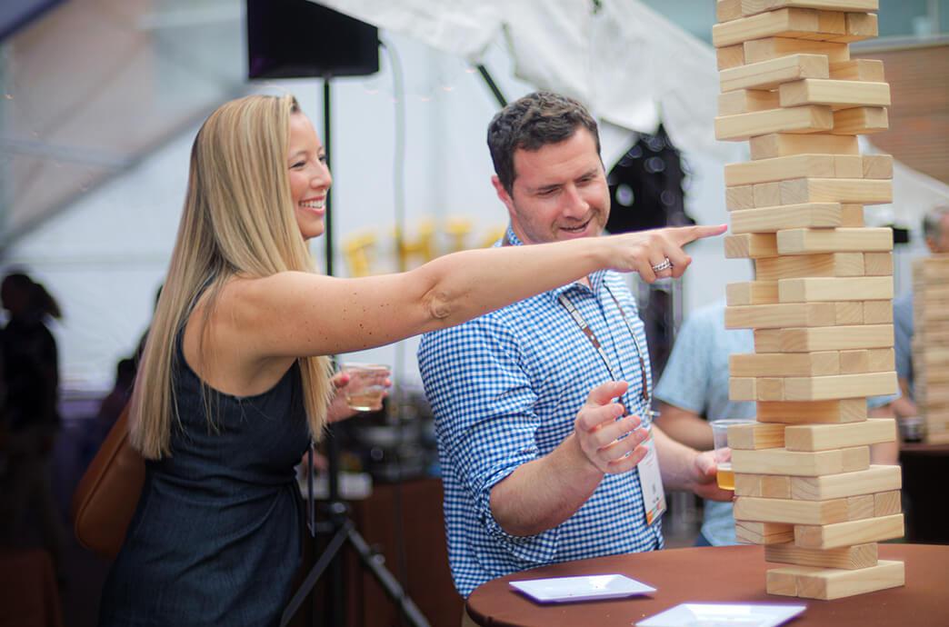 A woman and a man smile while playing a game of giant Jenga at an outdoor event. 