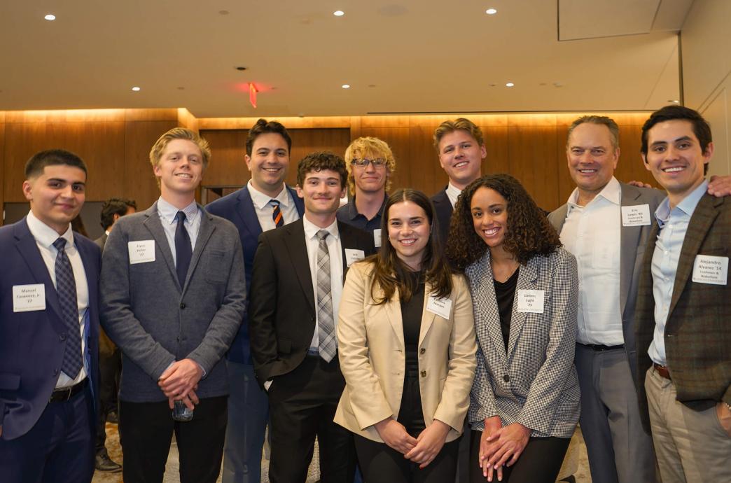 A group of event attendees, including men and women, dressed professionally posing for a photo, all wearing name tags and smiles.