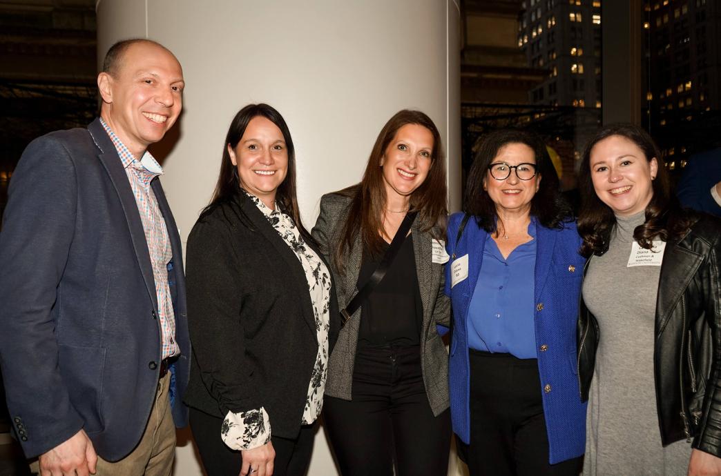 Four women and one man stand beside each other for a photograph in a dimly lit room.