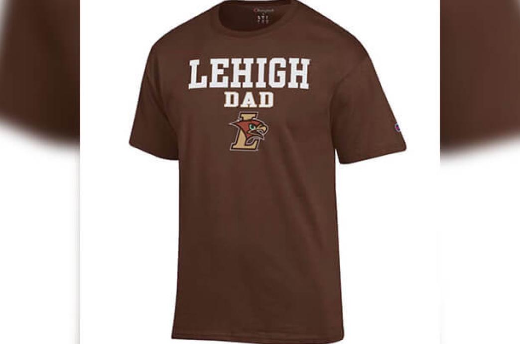 A product image of a brown tshirt with a small Champion logo on the sleeve and “Lehigh Dad” spelled on the front in white above an LHawk logo