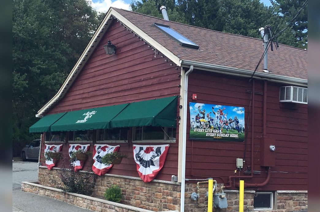 A brown building with a pitched roof and green awning has red, white, and blue banners hanging on the windows outside.