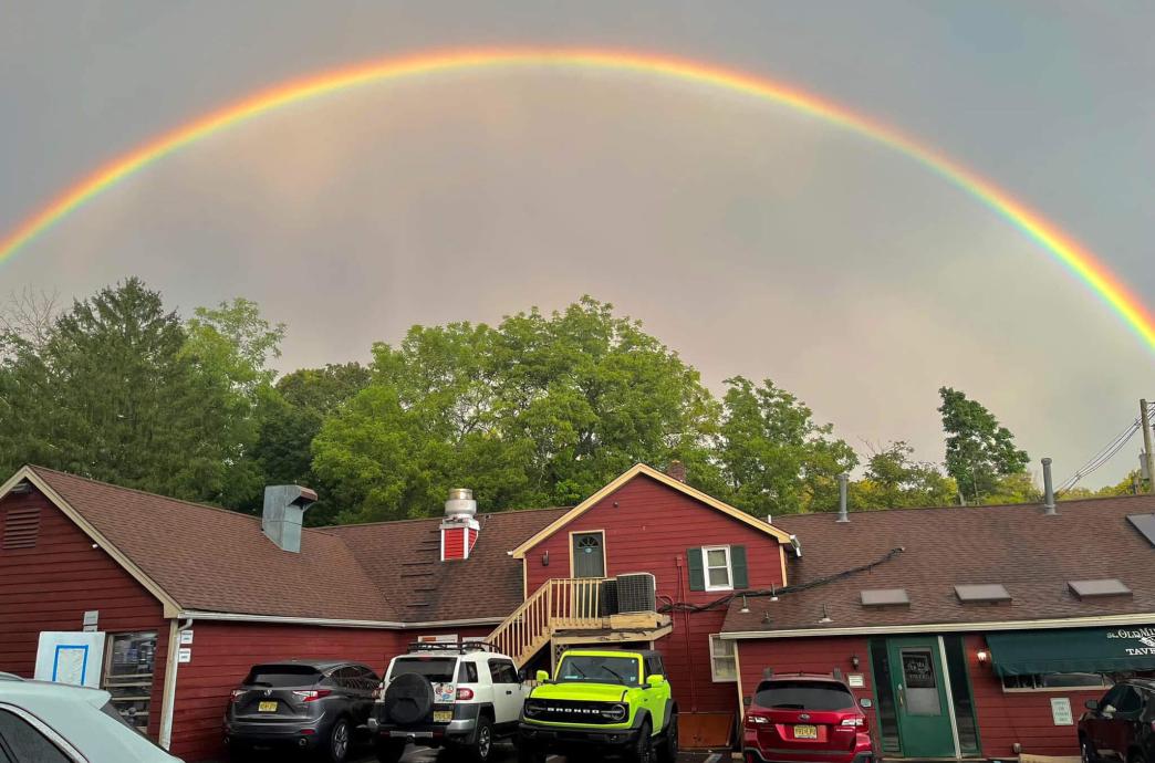 A wide shot of the entire Old Mill Tavern building with a bright rainbow reaching across the entire sky above it.