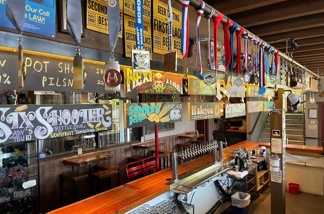 A view from behind the bar shows medals hanging from a bar above and colored signs with fun graphics for different beer options.