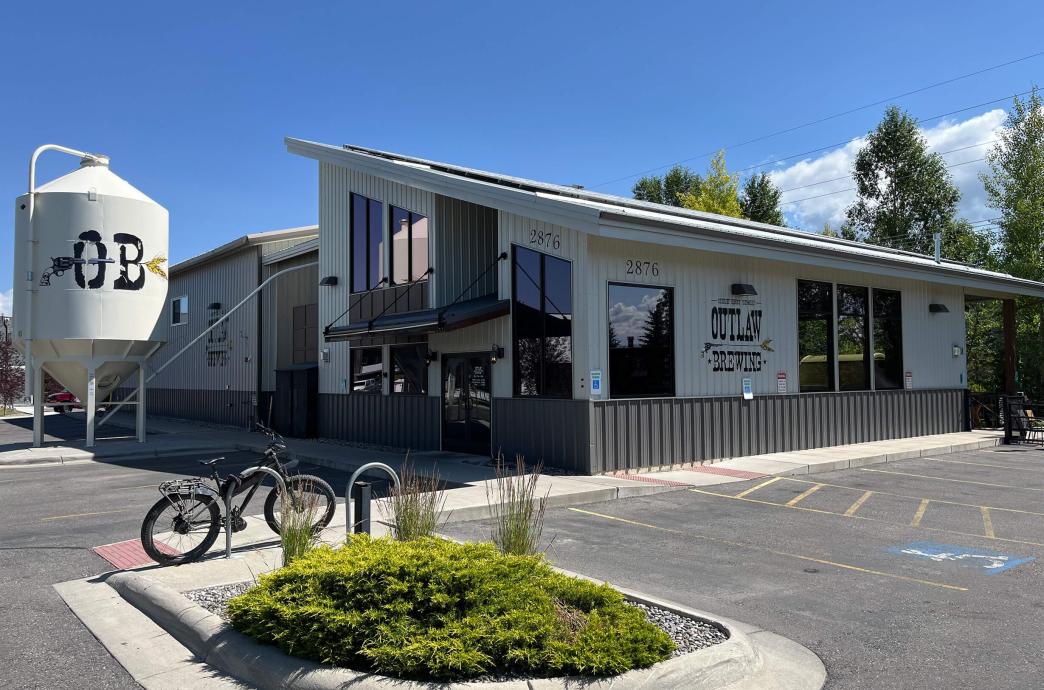 An exterior view of Outlaw Brewing, with white siding, a slanted roof, and a large vat outside reading “OB.”