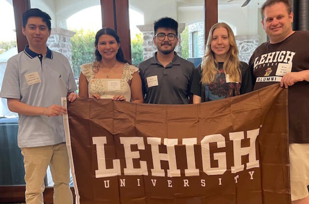 Group of five smiling people holding a Lehigh University banner indoors.