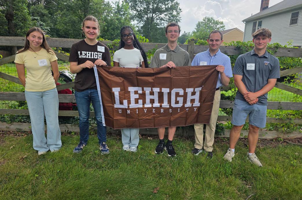Group of six smiling people holding a Lehigh University banner outdoors