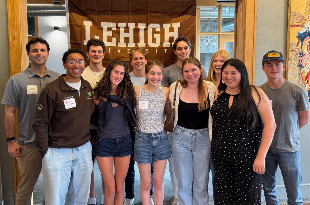 Group of 11 smiling people standing indoors in front of a Lehigh banner.