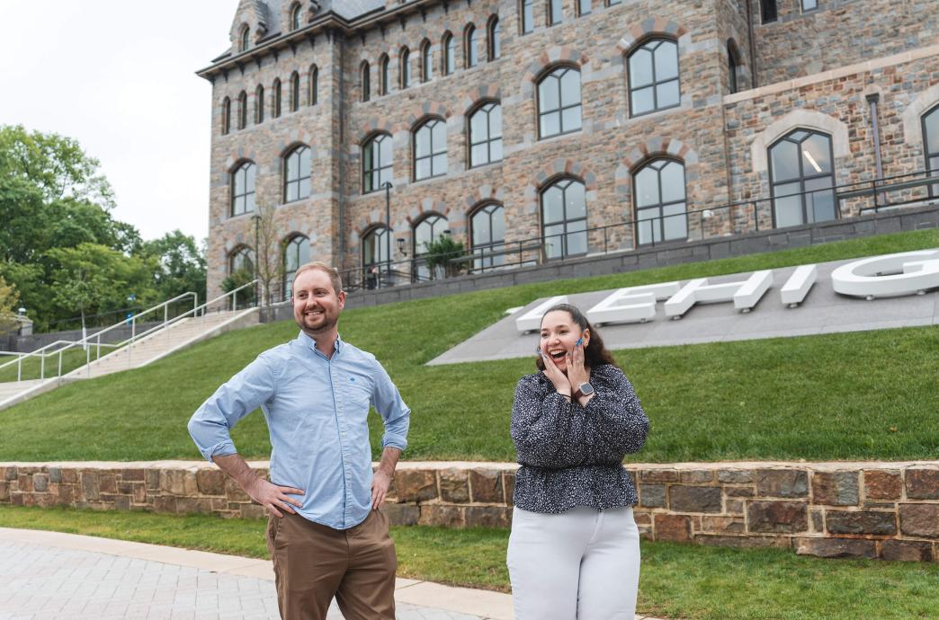 After their proposal, the couple stands in front of the Clayton UC with Anderson showing surprise with both hands on her face and smiling.