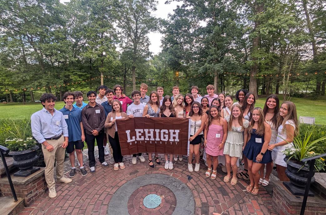 Group of 30 smiling people holding a Lehigh banner outdoors.
