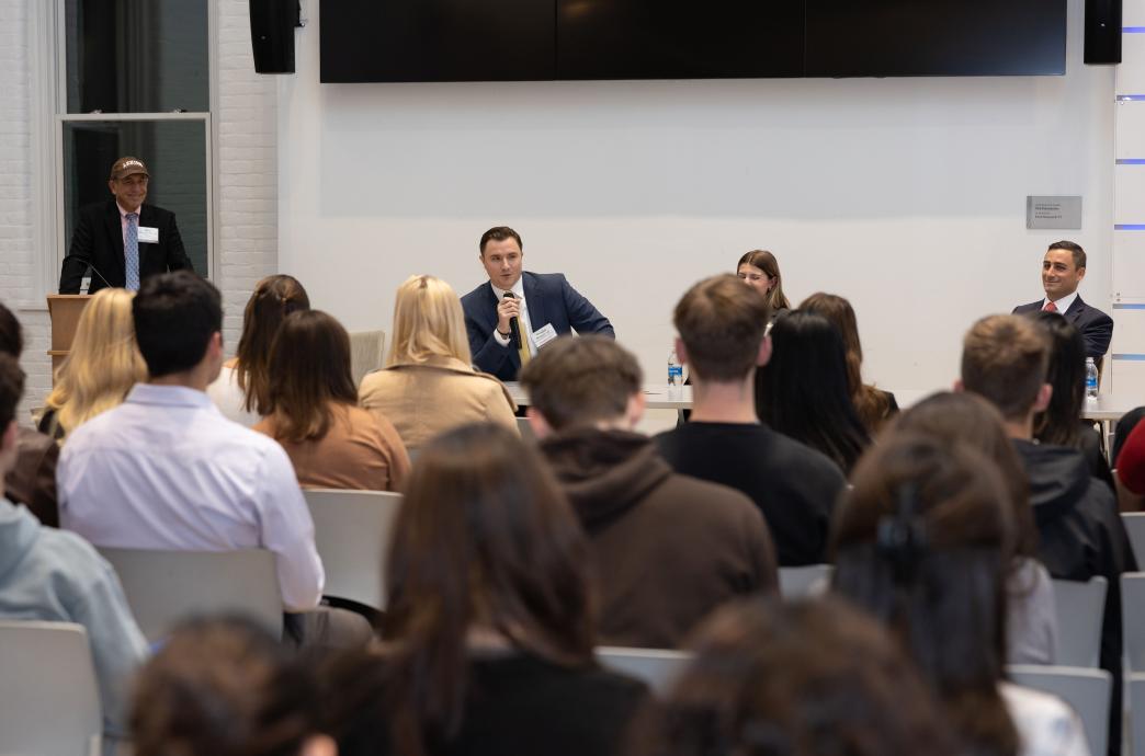 Noel Johnson, Nick Marcello, and Doug Moquet sit at a table in front of a room full of attendees; Doug is holds the mic. 