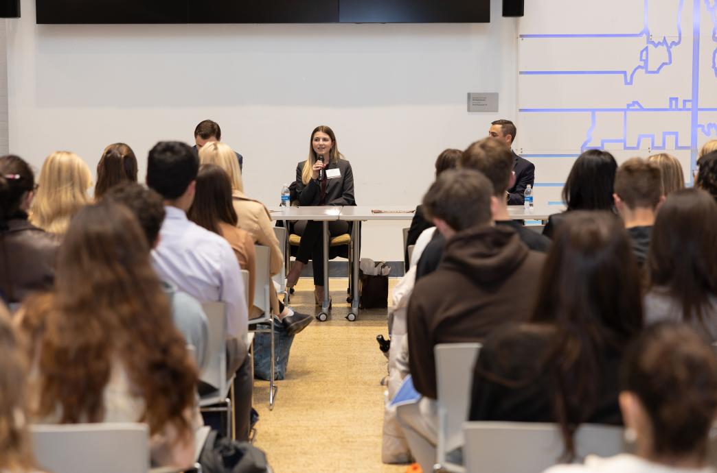 Noel Johnson, Nick Marcello, and Doug Moquet sit at a table in front of a room full of attendees; Noel holds the mic. 