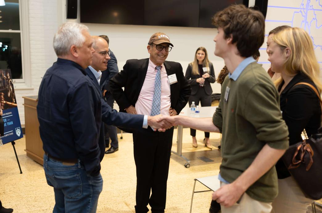 A group of people stand in a circle and chat. Barry Glickman is among them wearing a black suit and a brown Lehigh hat.