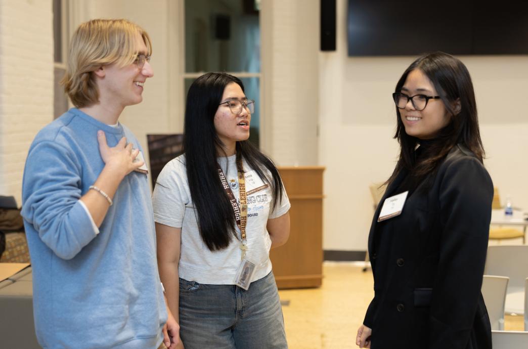 Three students stand casually in a semicircle chatting; Anna Van Riesen is among them in a t-shirt in jeans. 