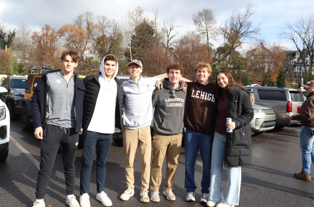A group of students smile while tailgating; one of them wears a Lehigh sweater while another next to them wears a Lafayette one.