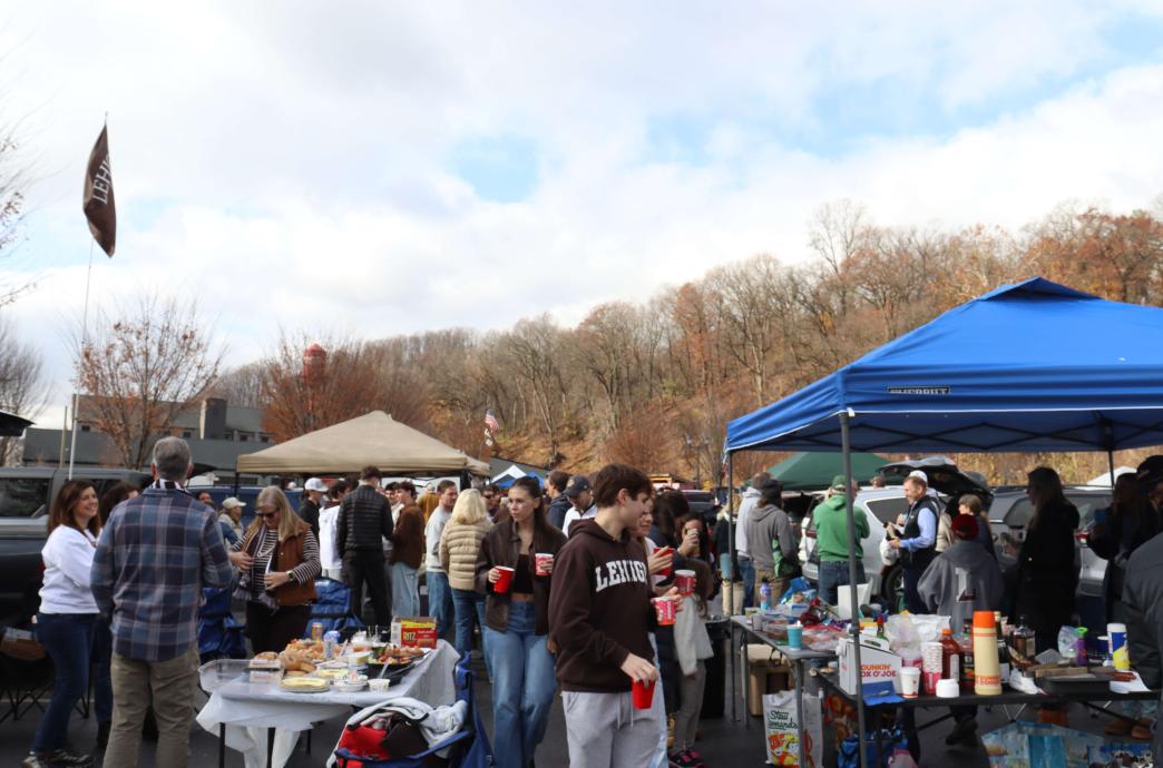 A large group of Lehigh fans of all ages tailgate. The sky is clear and light; the trees have lost almost all their leaves.
