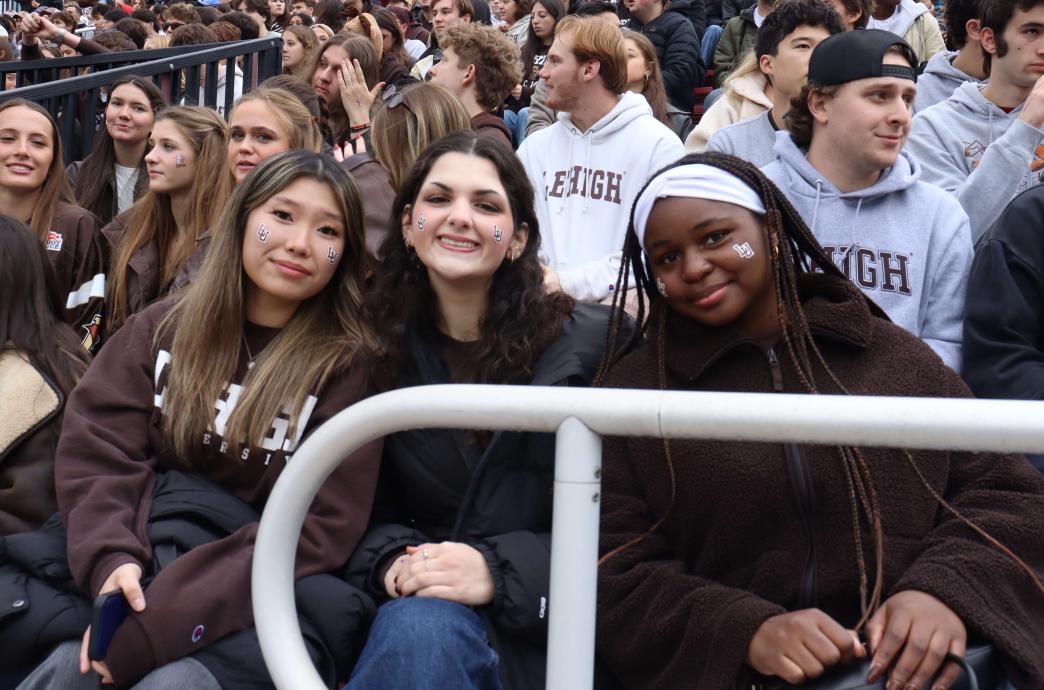 Three young women smile while sporting Lehigh colors; tiny 'LU' stickers are on their cheeks.