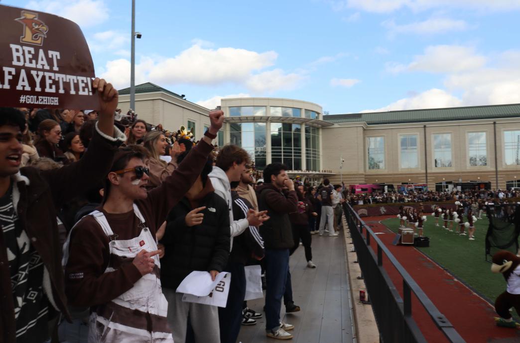 Shot of the crowd watching the game. Young men in Lehigh colors hold up a 'Beat Lafayette' sign; one of them painted his face.