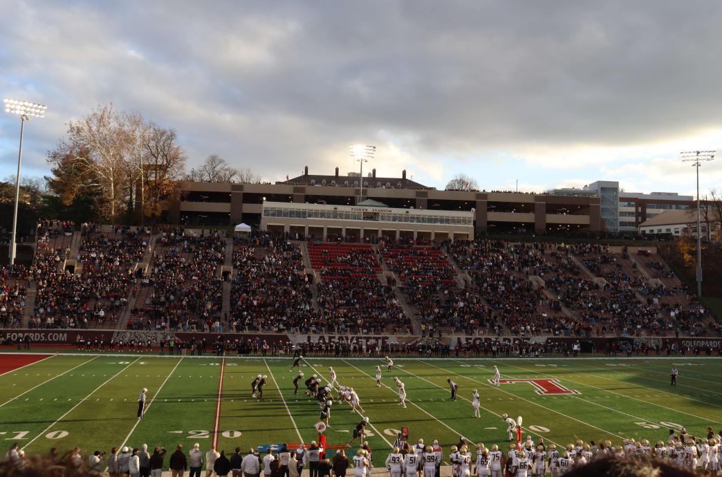 Shot of the field before a play. The sky is clear, the stadium is full, and the players from both teams stand facing each other.