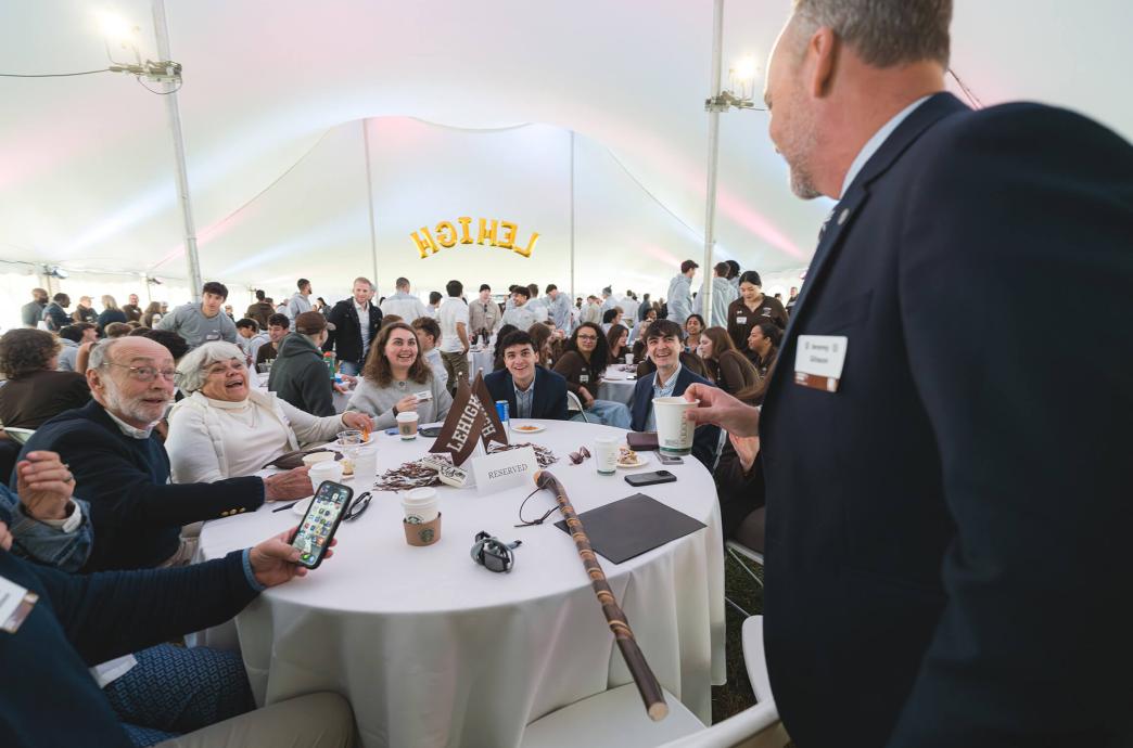 Jeremy Gibson, holding a coffee cup, leans in to talk to a table where a family of different ages is seated under a large white tent.