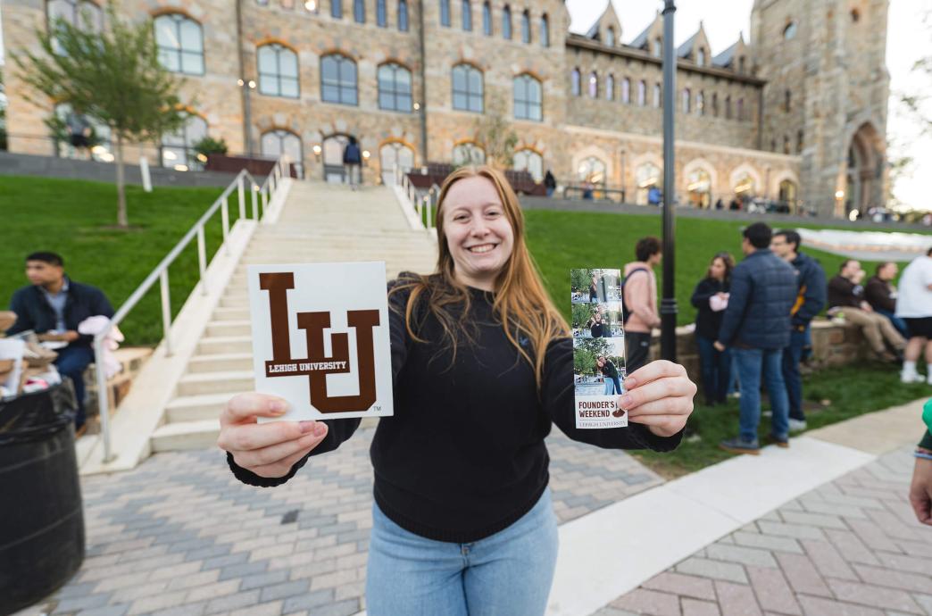 In front of the Clayton UC, a woman holds a large LU sticker inon hand and a photobooth printout in the other.