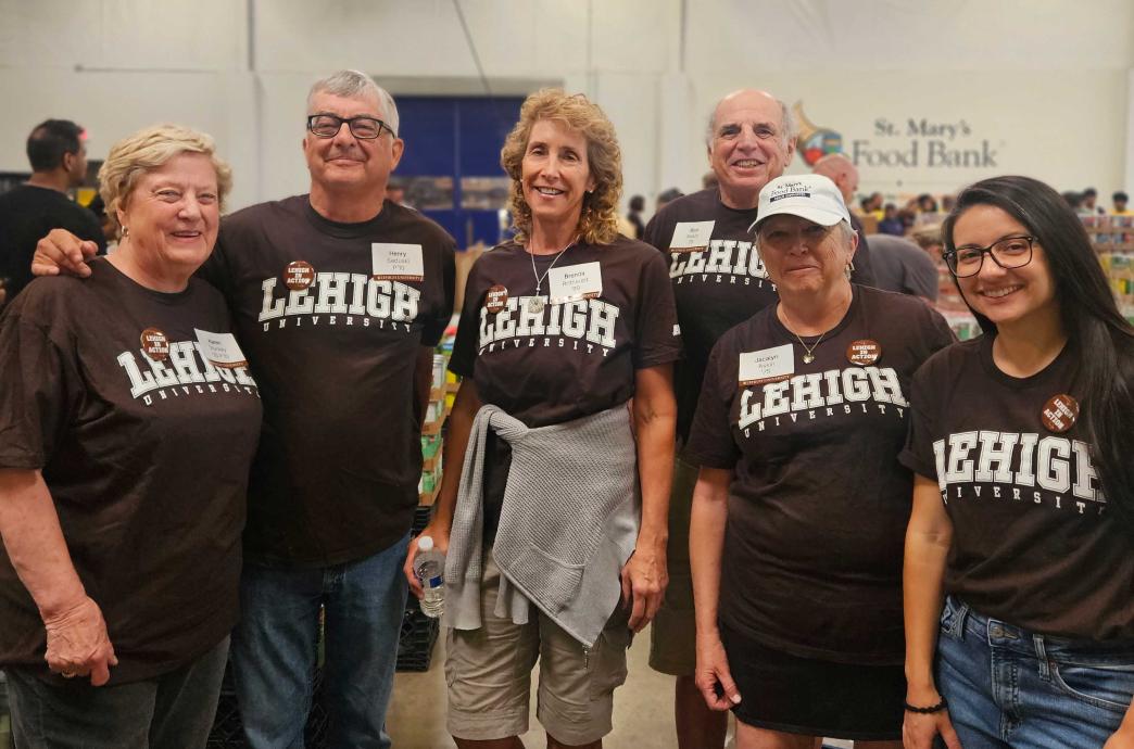 Six volunteers wear matching brown Lehigh shirts and Lehigh pins. Behind them the St. Mary's Food Bank logo is visible.