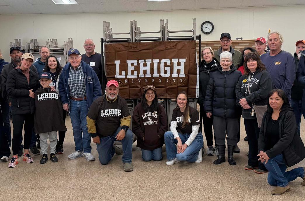 A large group of volunteers stand near a Lehigh banner and smile. Several wear matching brown Lehigh shirts. 