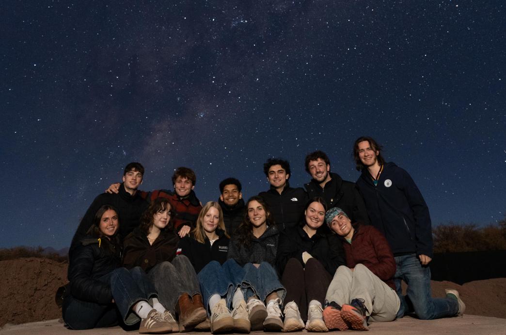 A group of students stand together in the Atacama Desert at night. The sky is bright with stars above them.