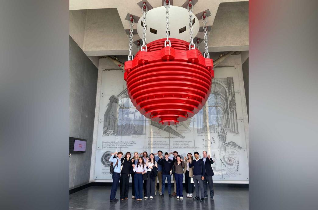 A group of students stand under a bright red tuned mass damper in the Chilean Chamber of Construction.