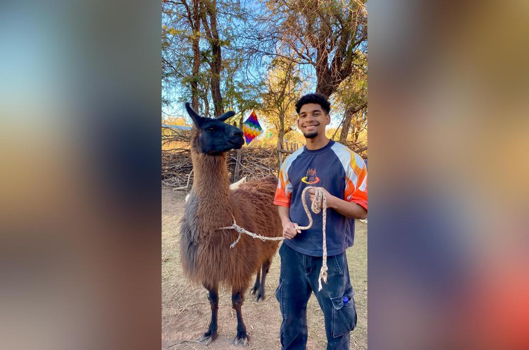 Michael stands next to a large brown and black llama and holds its rope leash.