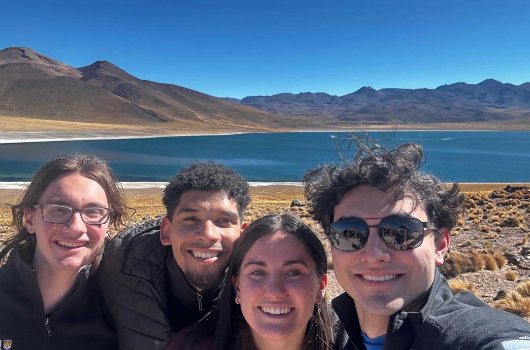 A group of students smile in front of a lagoon in the mountains.