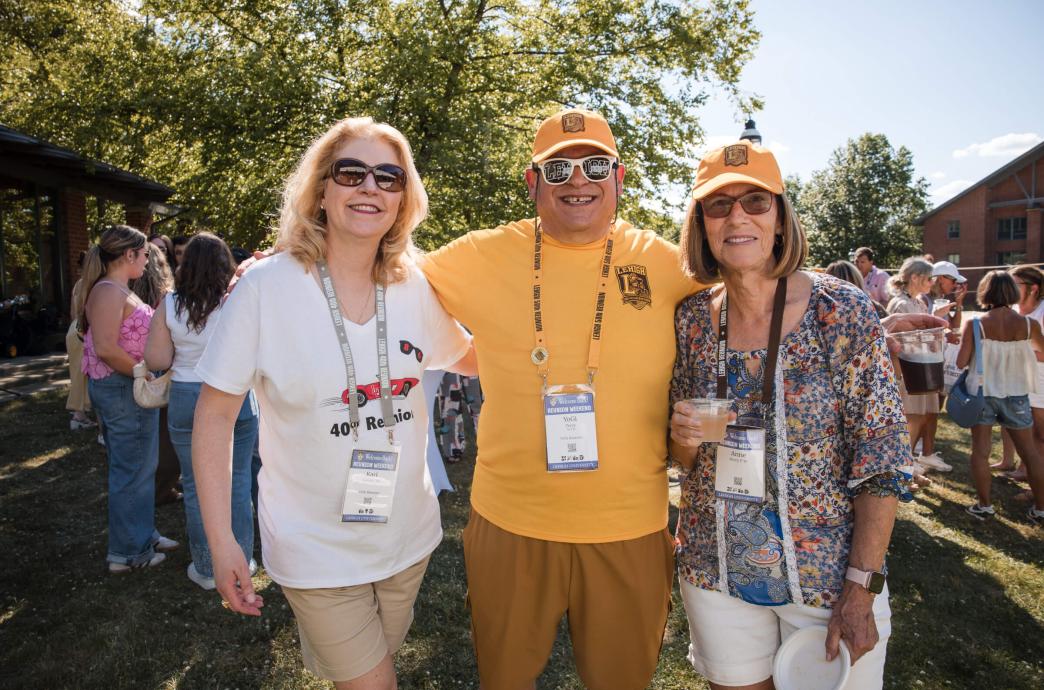 Three alumni stand together and smile while wearing Lehigh merch and sunglasses.