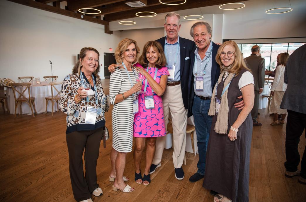 A group of alumni stand together and smile. They each wear light blue a lanyard with their name on it.
