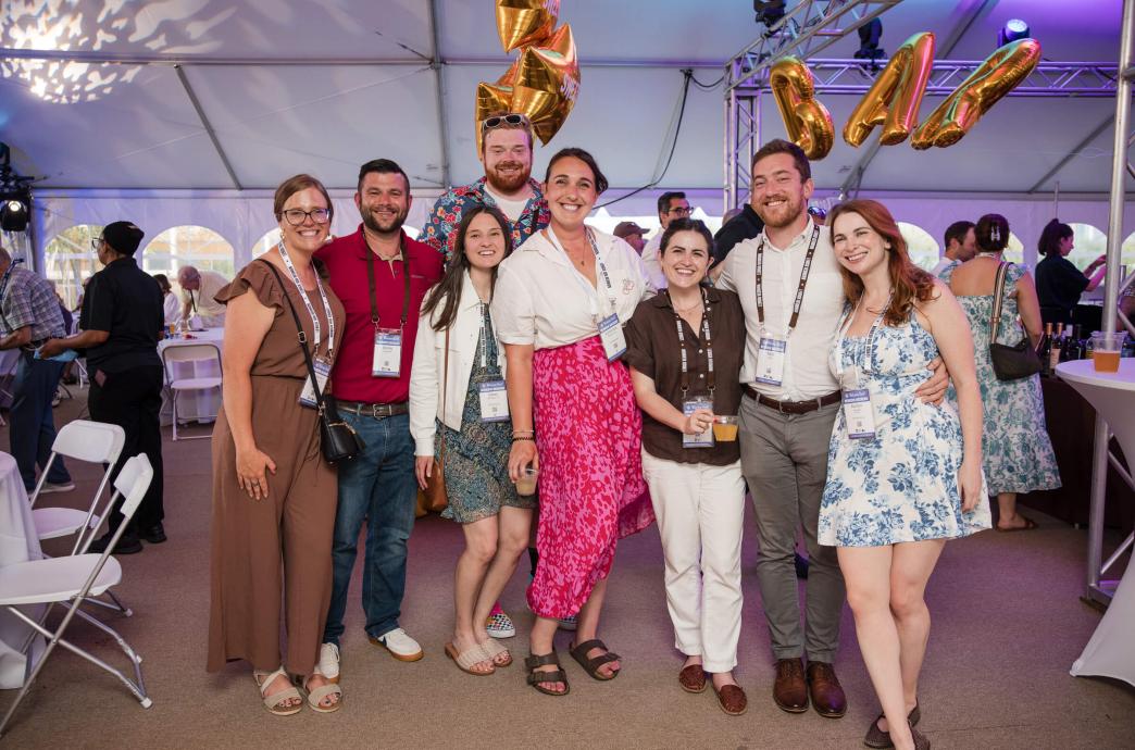 A group of alumni stand together and smile at a Reunion event in front of balloons that spell out 'bar.'