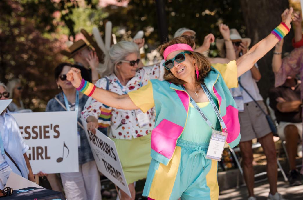 A woman dances while wearing bright, 80s style athletic wear, including a pink sweatband and rainbow wristbands.