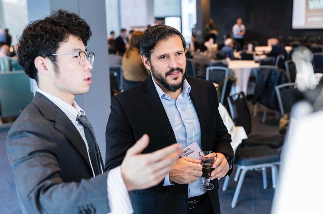 Two men in suits talk animatedly in a room full of tables