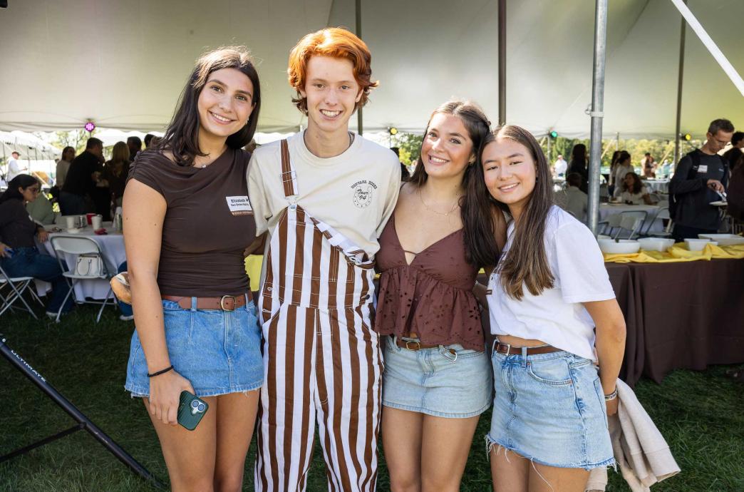 Four young students pose together under the tent at tailgating. 