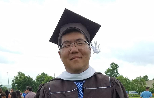 John Lim stands in his cap and gown