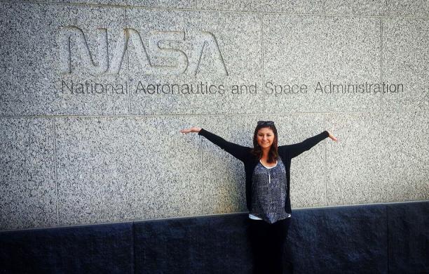 Kristina Gonzalez standing infront of a wall that reads NASA, National Aeronautics and Space Administration