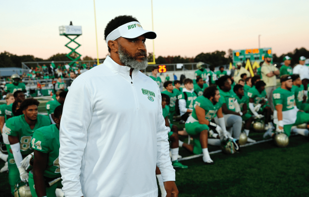 Bryant Appling stands on the sidelines with his football team kneeling in the background in their green uniforms.