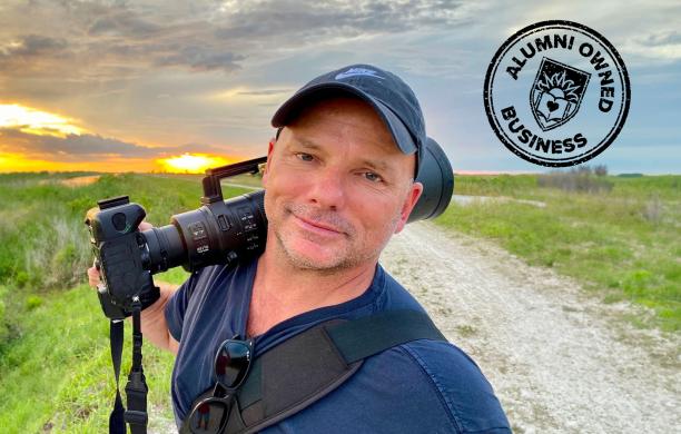 Alumni Owned Business, Michael Patrick O'Neill smiling for a selfie with his camera with an expansive field behind him.