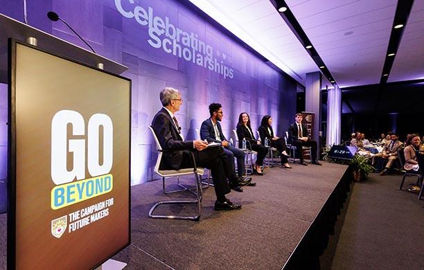 GO Beyond logo on a stage podium alongside a panel including President Helble and four students