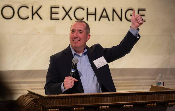 Award honoree stands at podium at the New York Stock Exchange with one hand holding a microphone and the other raised in the air