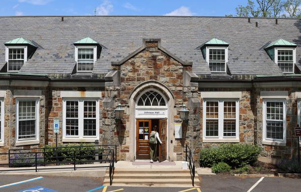 Student with backpack enters stone building with the words Johnson Hall marking the top of the two-door entry.